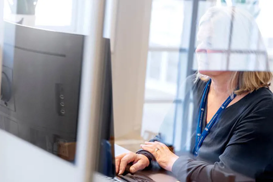 En person iført en hvit lue og blå skjorte som jobber på en bærbar datamaskin